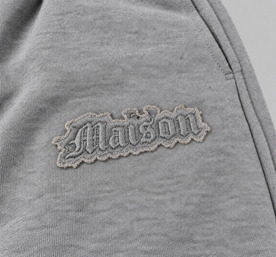 Signature Sweatpants Product V3 Grey Melange. Nahaufnahme des gestickten Logos auf den grauen Maison De La Rue Sweatpants.