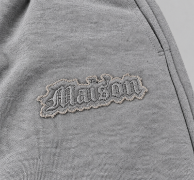 Signature Sweatpants Product V3 Grey Melange. Nahaufnahme des gestickten Logos auf den grauen Maison De La Rue Sweatpants.